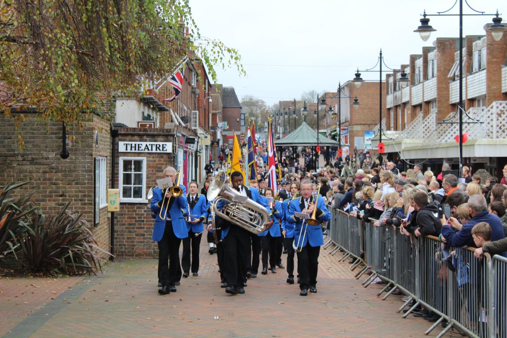 Brass band leading the parade down Church Walk next to a crowd watching
